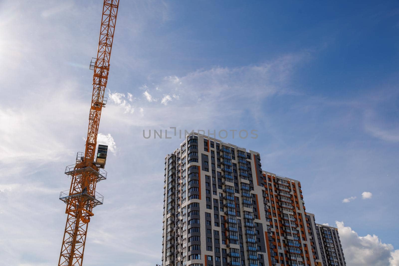 freshly built high rise apartment building near yellow crane on blue sky background with thin feathery clouds.