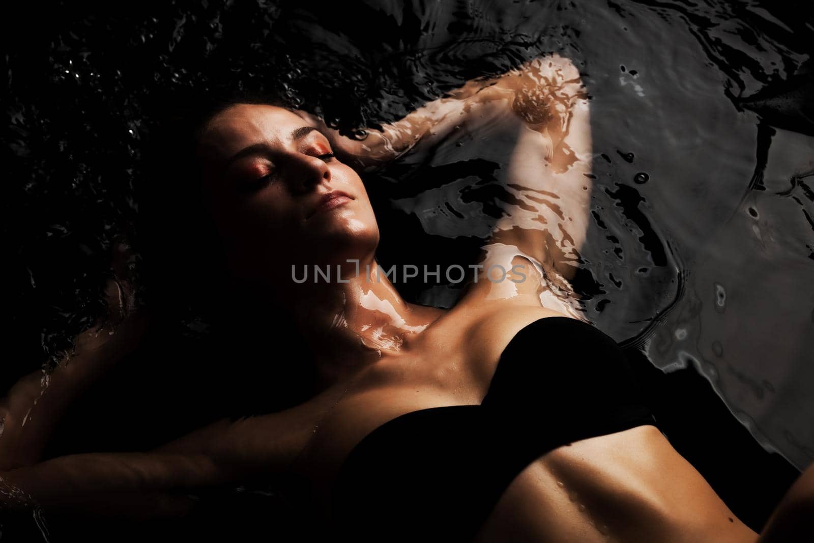 Beautiful caucasian girl in swimsuit lying in water with reflections on the surface. . by kokimk