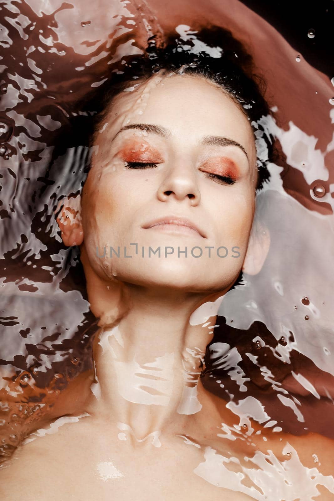 Underwater beauty portrait of a beautiful caucasian girl. Eyes closed. Red colored water.