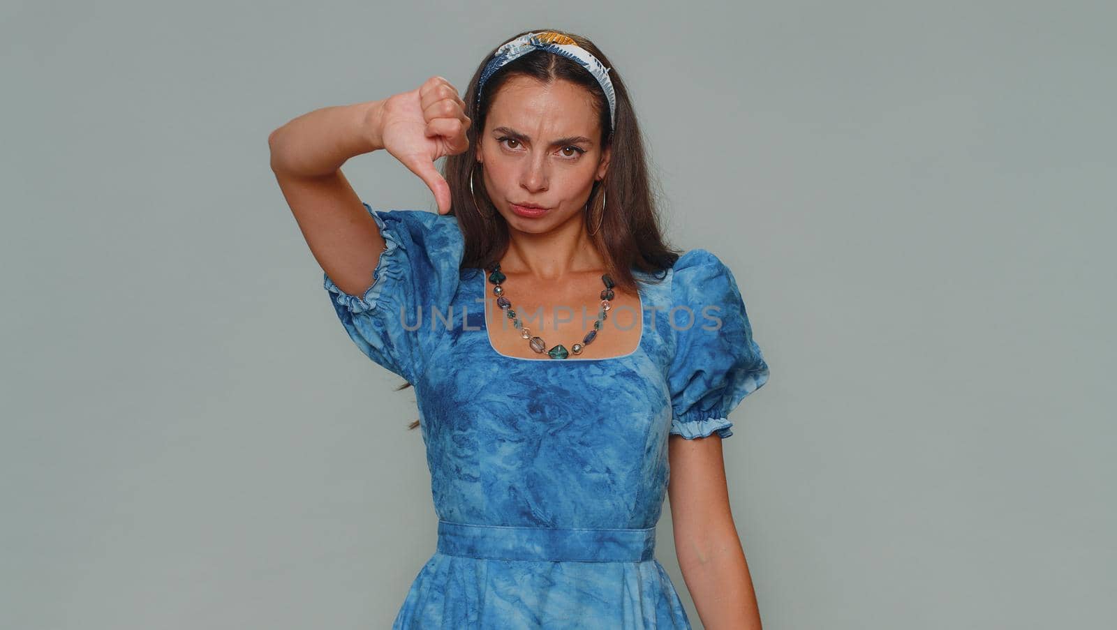 Upset lovely pretty young woman showing thumbs down sign gesture, expressing discontent, disapproval, dissatisfied, dislike. Adult stylish female girl isolated alone on gray studio background indoors