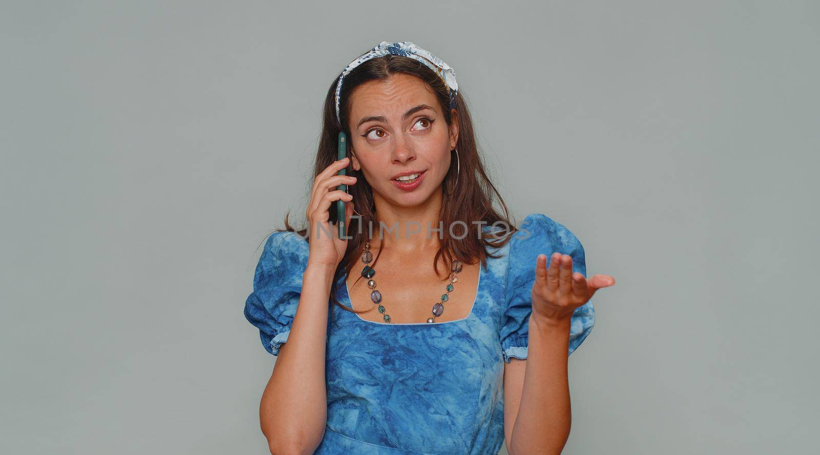Tired sleepy freelancer young woman talking on mobile phone with friend, making online conversation. Disinterested female girl having annoyed boring talk on smartphone on gray studio wall background
