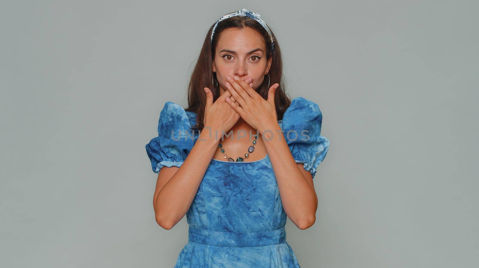 I will not say anyone. Frightened young woman closing her mouth with hand, looking intimidated scared at camera, gestures no, refusing to tell terrible secret, unbelievable truth. Adult female girl