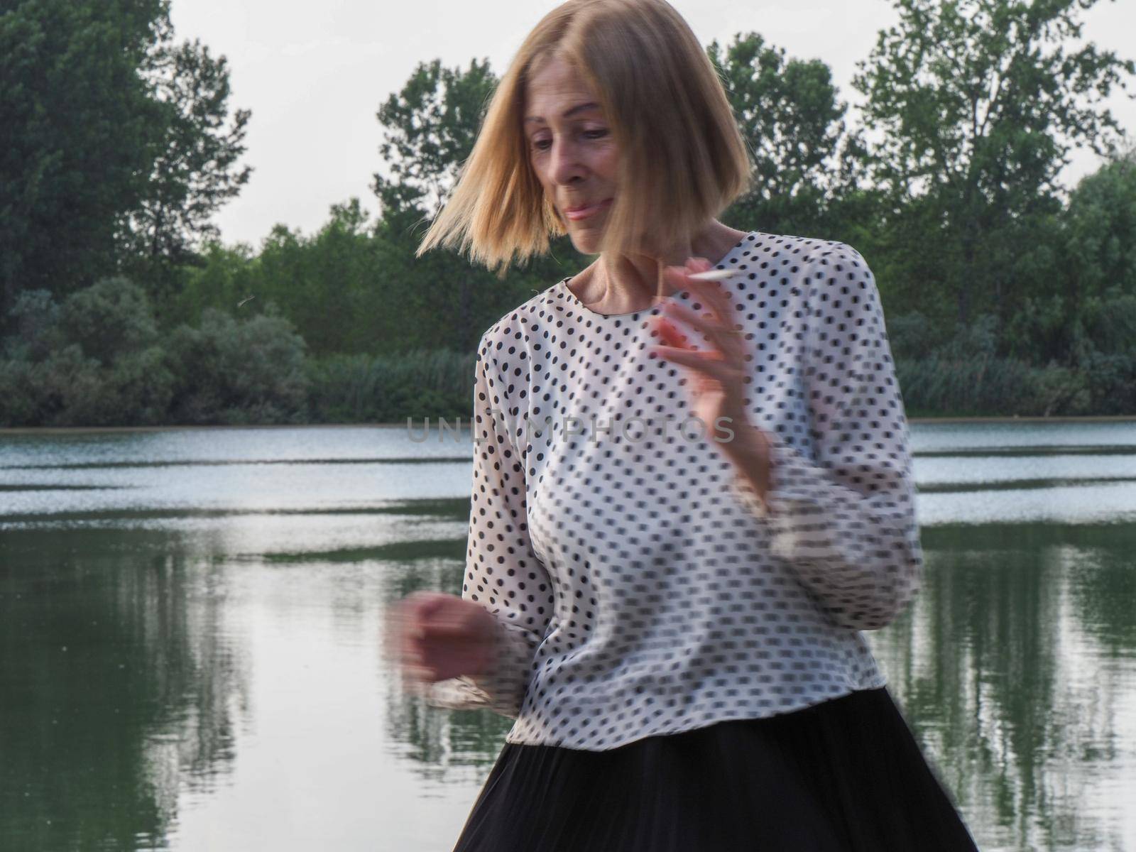 female pensioner having fun and smoking a cigarette in a park - aging free and wellness concept