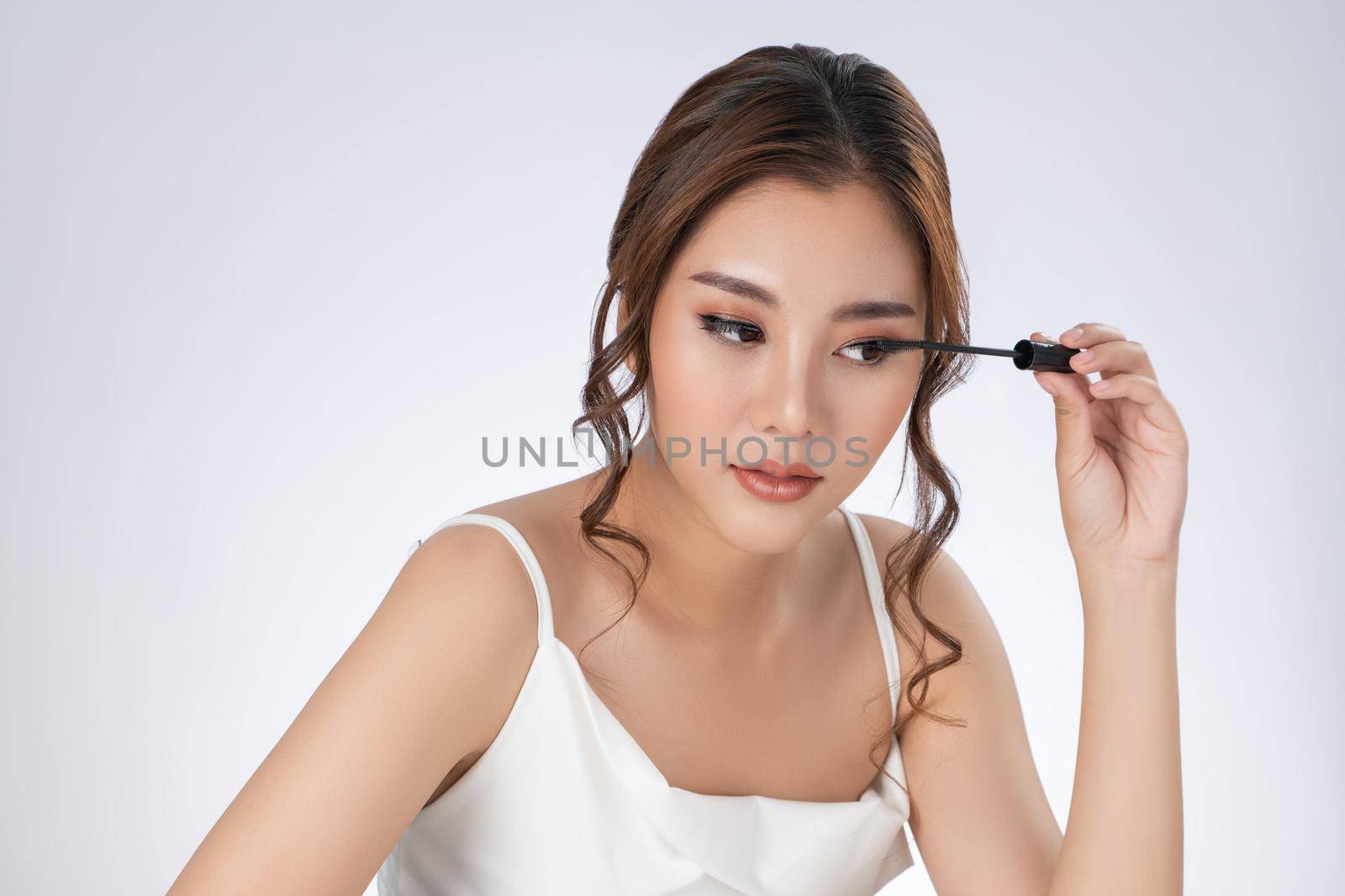 Gorgeous young woman putting black mascara on her long eyelashes with brush. Beauty cosmetic concept. Female model with perfect skin.
