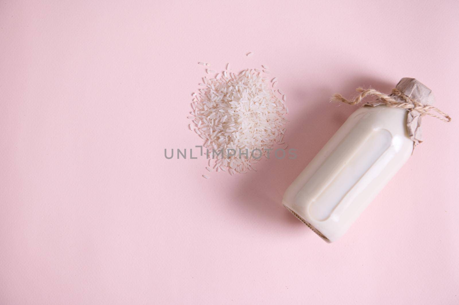 White rice, plant based, organic, raw vegan milk in a bottle, with kraft paper on the cap, tied with linen rope, isolated on a pink background. Copy the ad space. Healthy eating and veganism. Flat lay