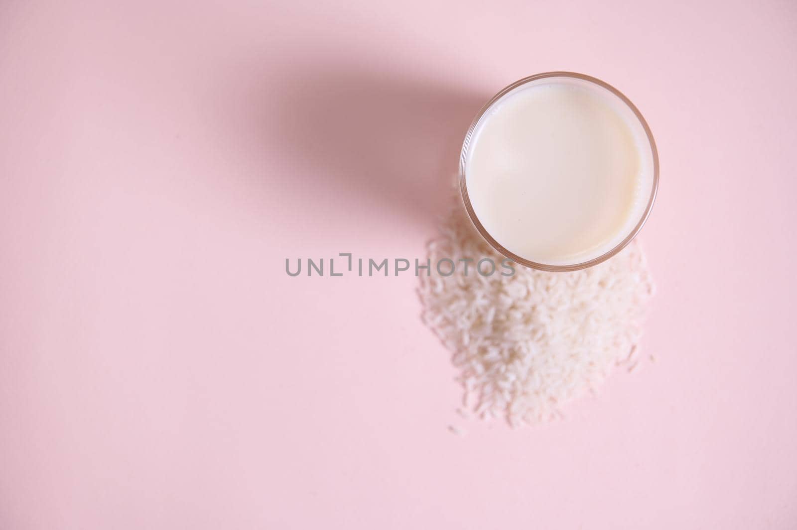 Flat lay. Still life with food and drink. Top view drinking glass of fresh organic, raw vegan, vegetable rice milk on pink background with copy advertising space. Healthy eating and veganism concept