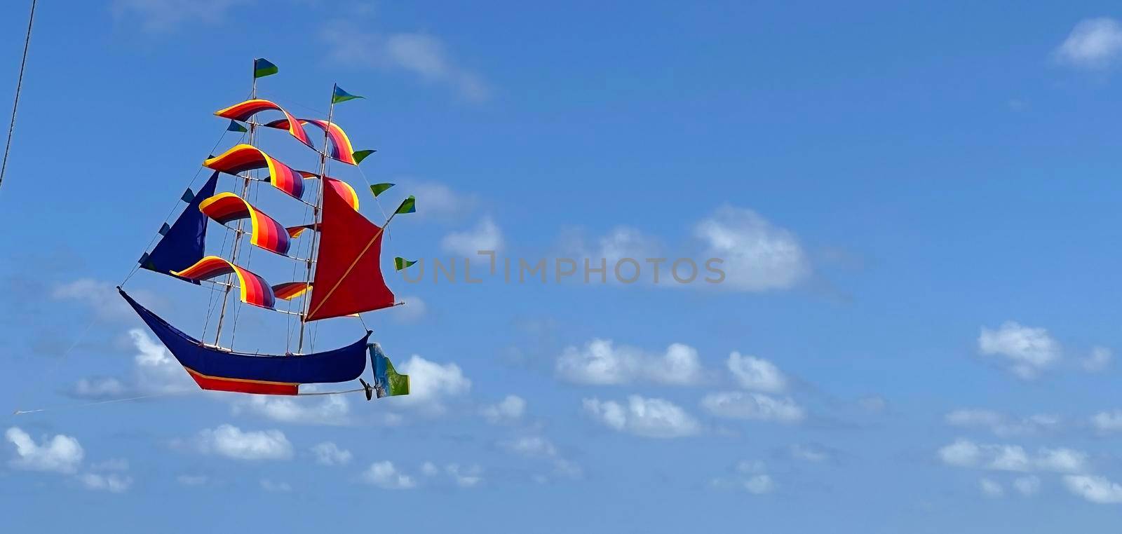 flying ship, rainbow colored ship kite flies on the blue sky and cloud by antoksena