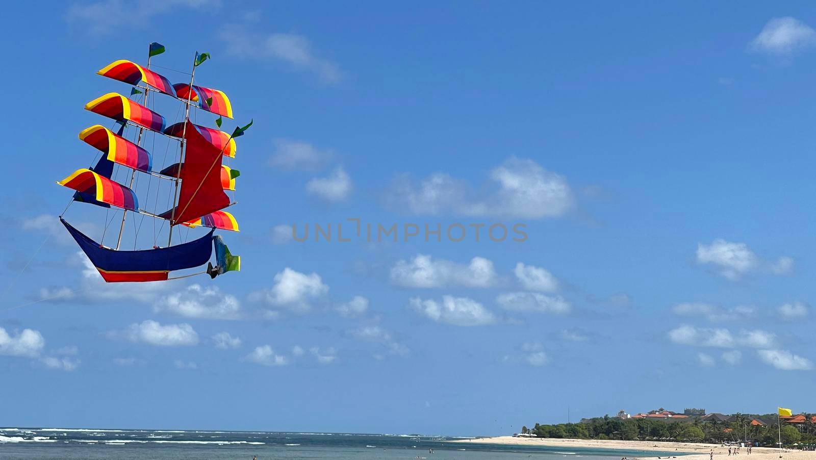 flying ship, rainbow colored ship kite flies on the blue sky and cloud in the beach