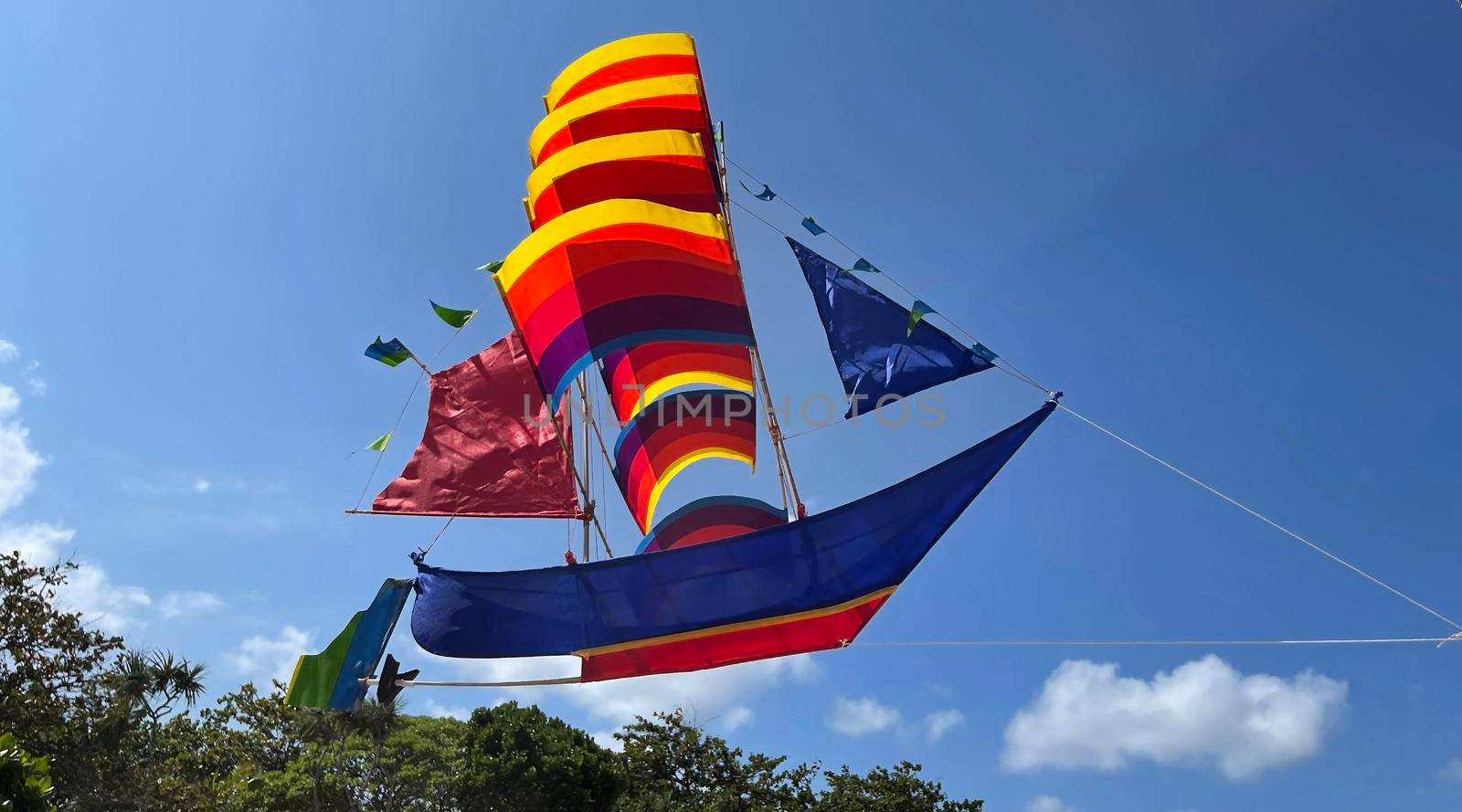 flying ship, rainbow colored ship kite flies on the blue sky and cloud in the beach