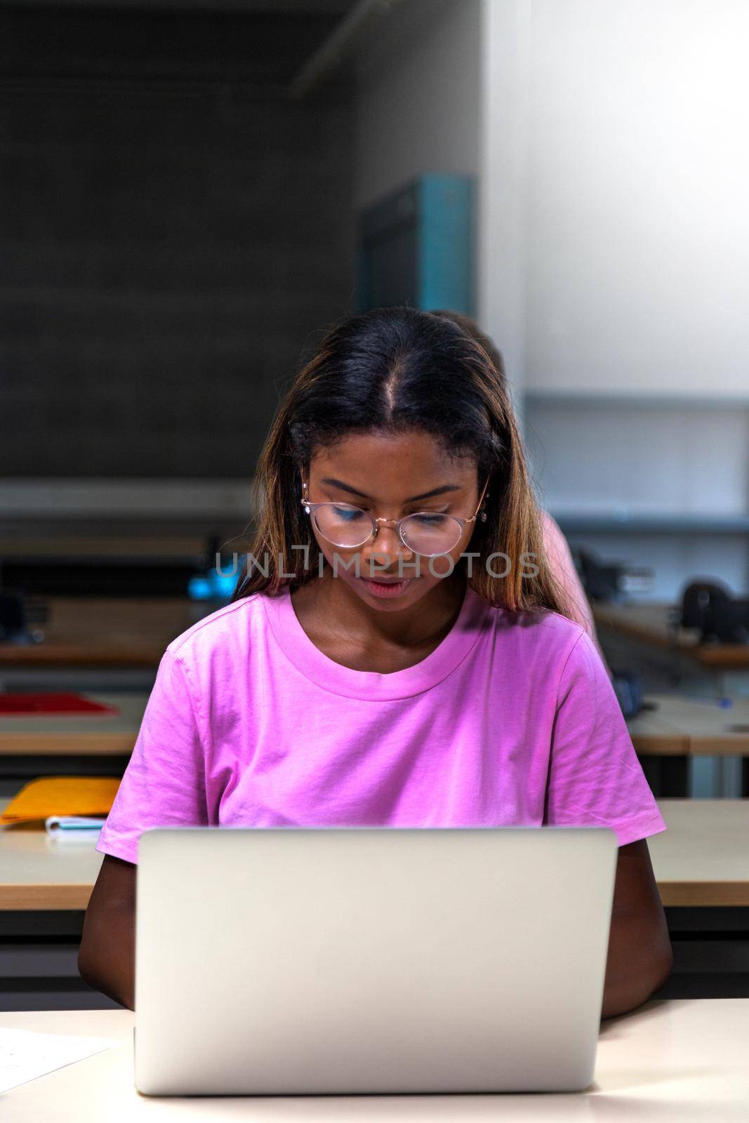 African american college student using laptop in class. Teen female black high school student doing homework. Vertical. by Hoverstock