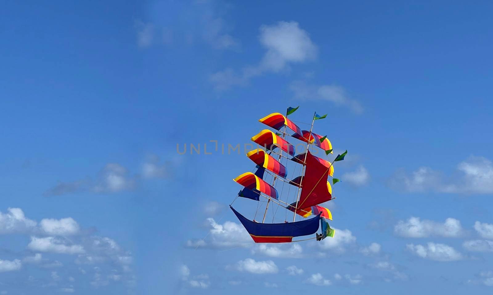 flying ship, rainbow colored ship kite flies on the blue sky and cloud in the beach