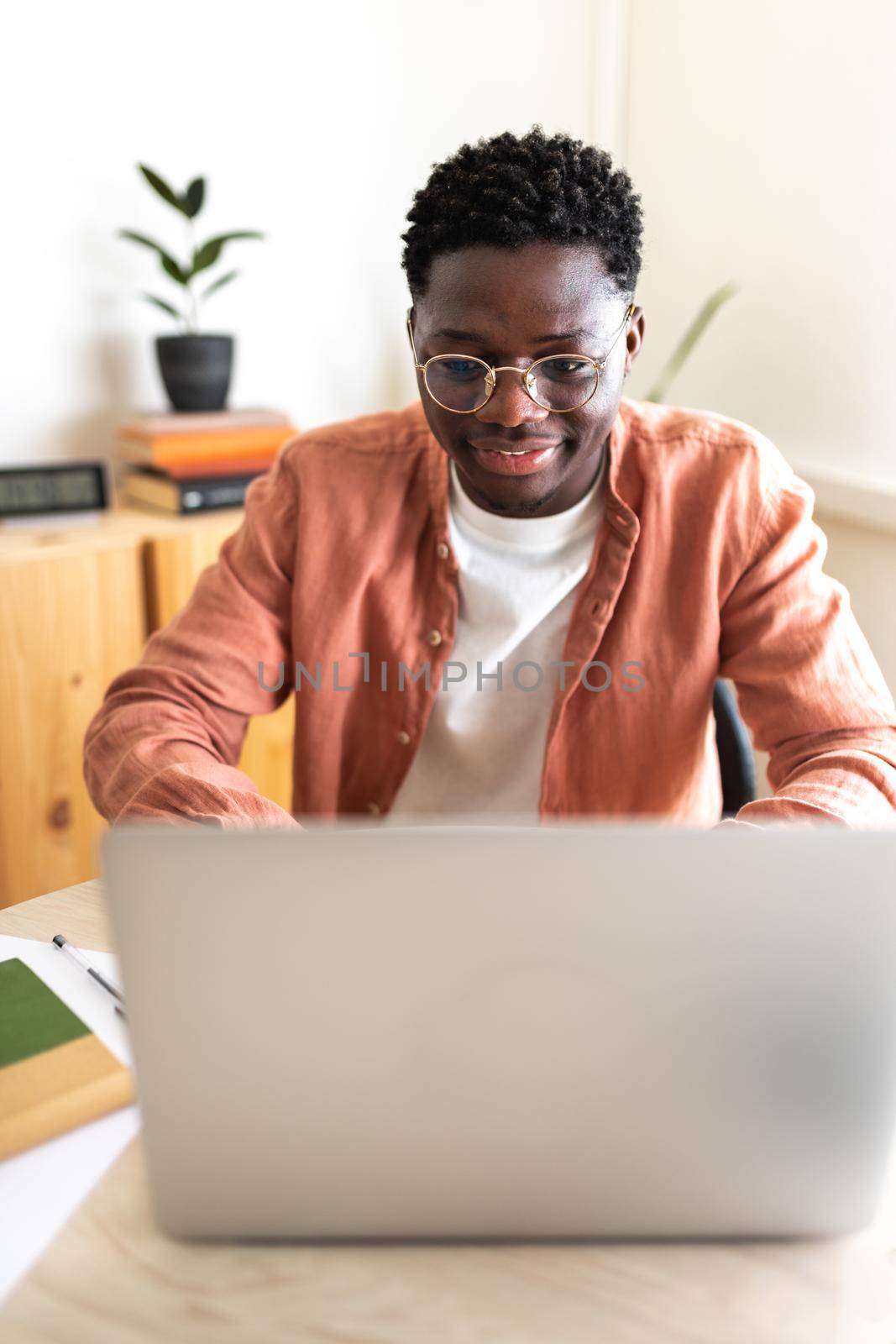 African American male college student studying at home using laptop. Vertical image. Education and technology