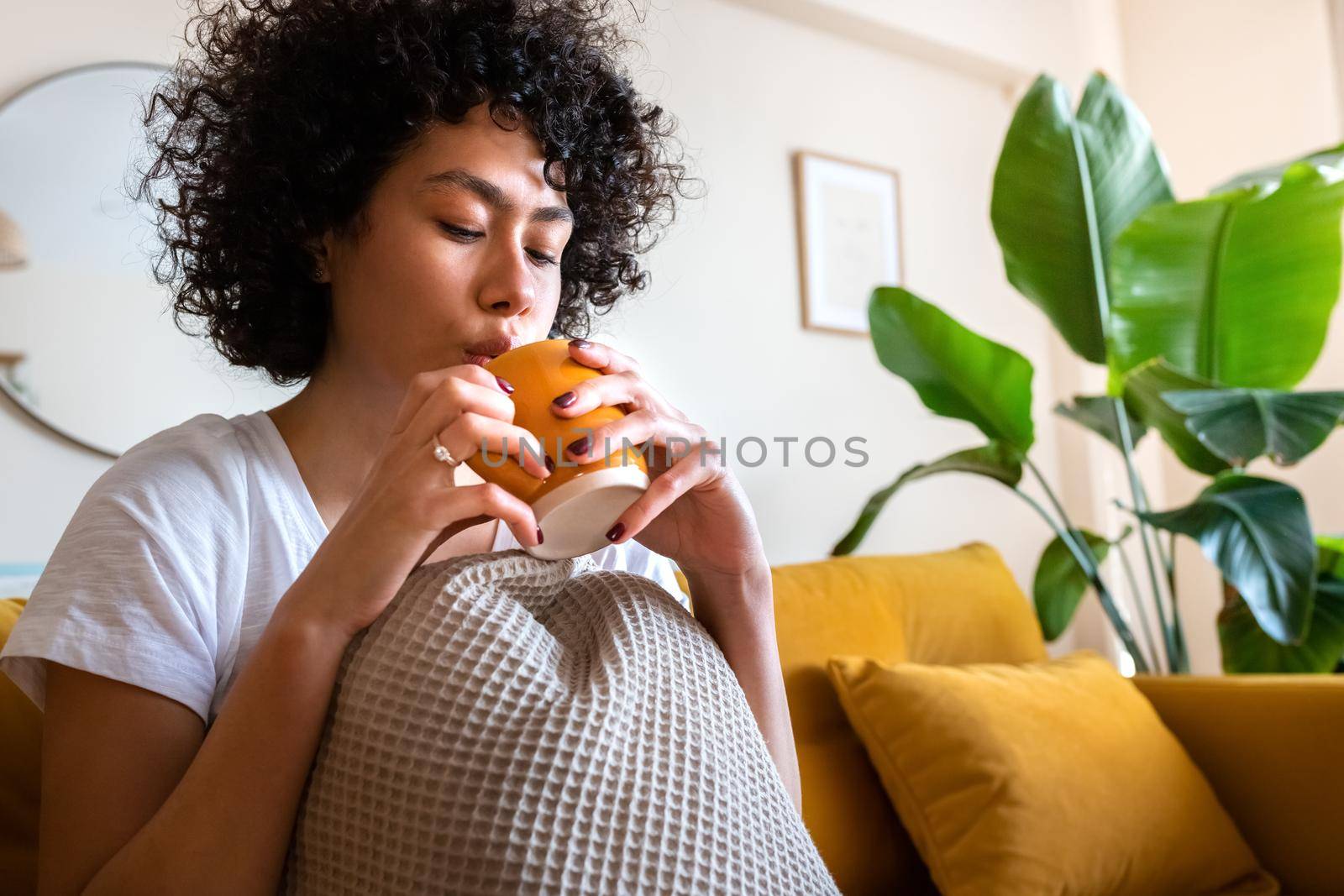 Young African American woman blowing on hot tea to cool beverage off. Relaxing at home sitting on the couch drinking coffee. Copy space. Lifestyle concept.