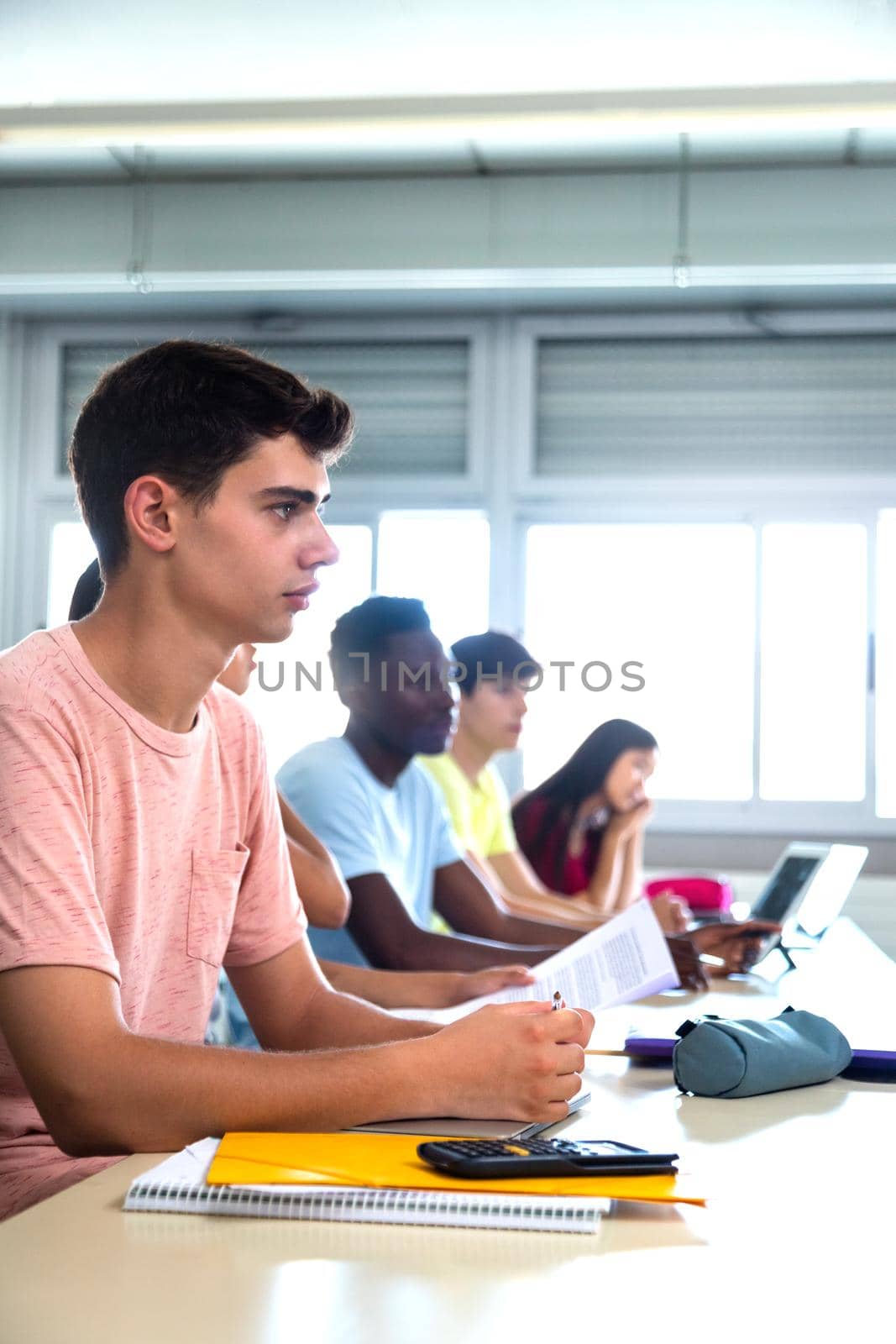 College male student in class listening to teacher. Multiracial teen high school students in classroom listen to lecture. Copy space. Vertical. Education concept.