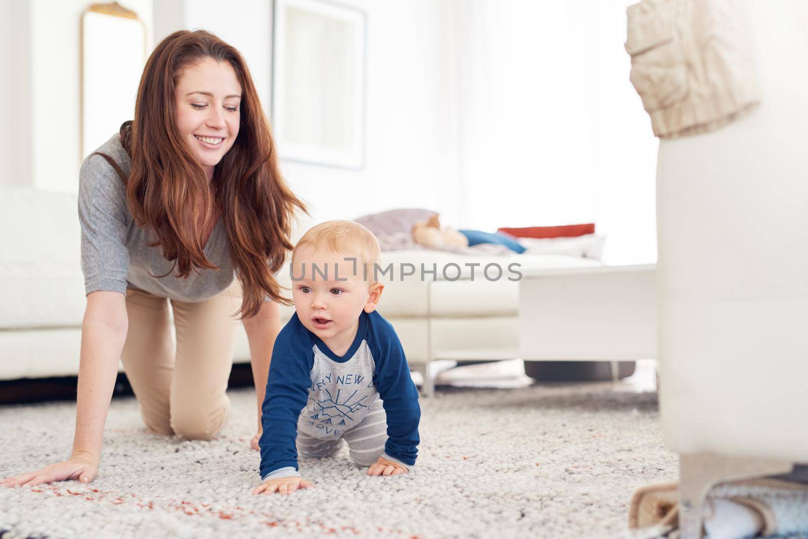 Exploring the world with Mom. a mother and her baby boy crawling together at home. by YuriArcurs