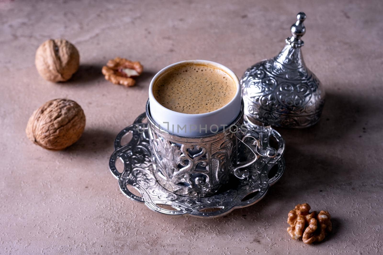Small beautiful traditional cup with Turkish coffee stands on a beige background. Walnuts lie next to a coffee cup. Selective focus.