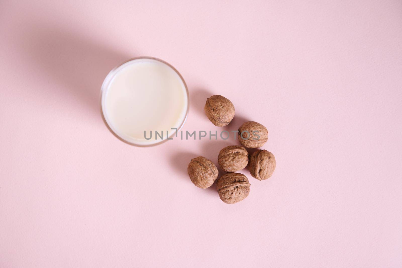 Flat lay with a vegetable milk in a drinking glass, alternative lactose free drink and a handful of organic wholesome walnuts on a pink background with advertising copy space. Healthy food and drink