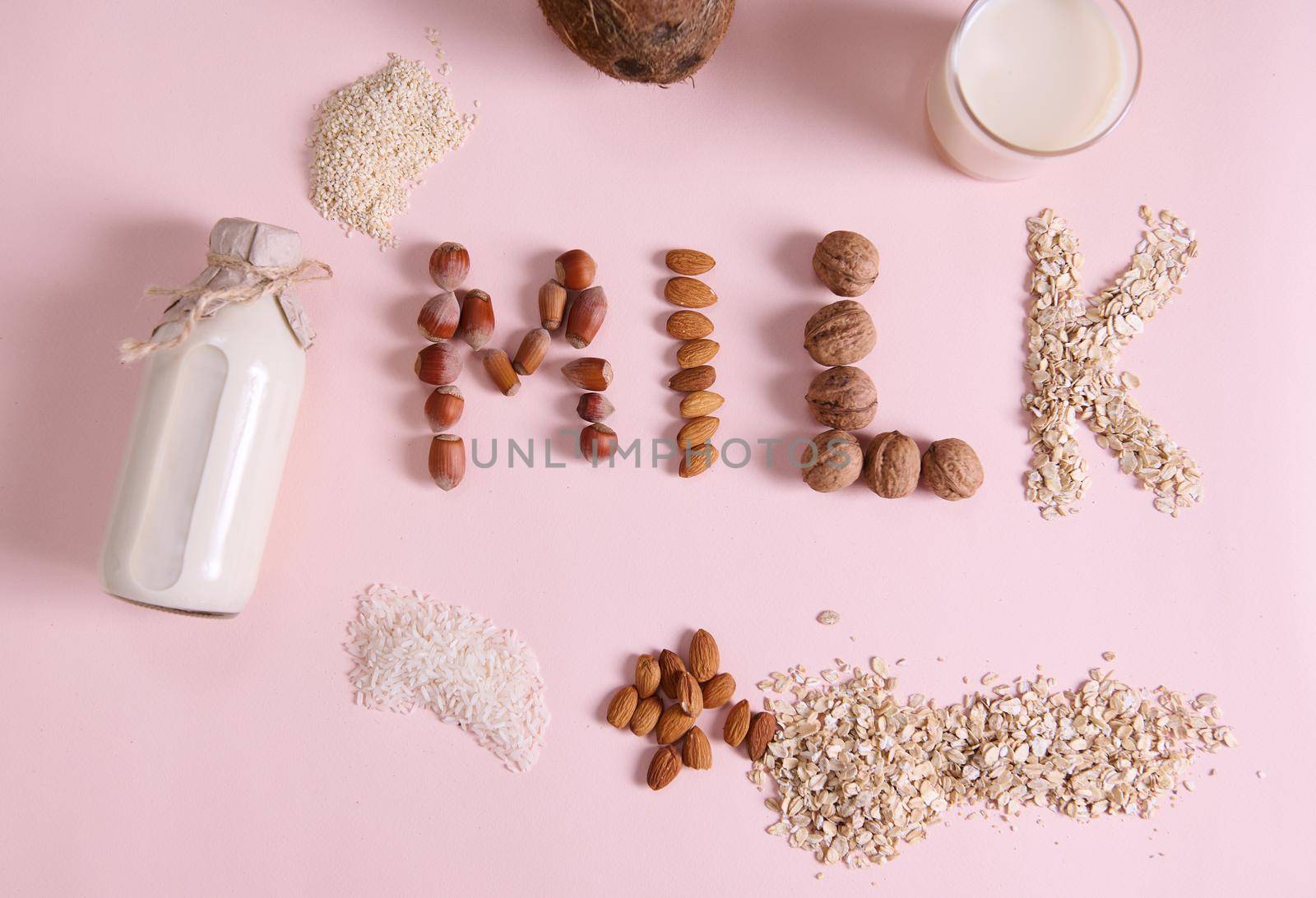Flat lay Lettering Milk on pink background, using wholesome ingredients, cereals, nuts and seeds. Bottle of vegetable, alternative, dairy free milk made from White Rice Oatmeal sesame Almonds Coconut