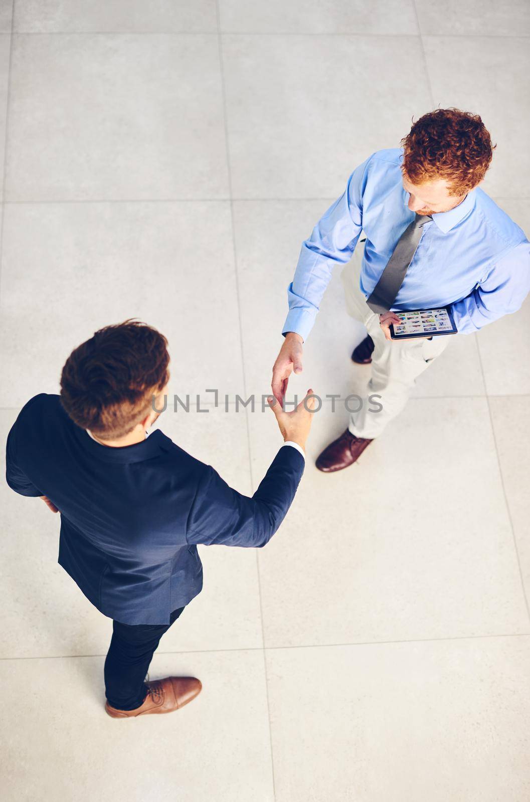 Its a pleasure to welcome you to our company. High angle shot of two businessmen shaking hands in an office. by YuriArcurs