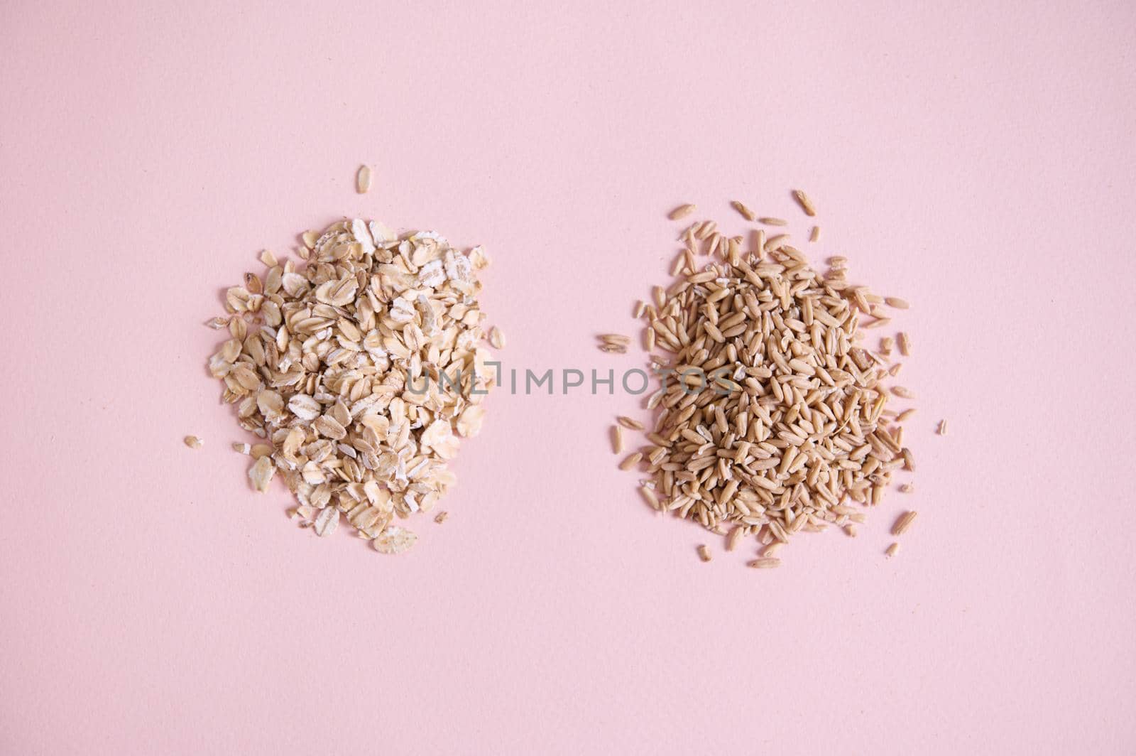 Flat lay. Heap of organic wholesome cereals oatmeal groats and oat-flakes scattered on pink background with copy space. by artgf