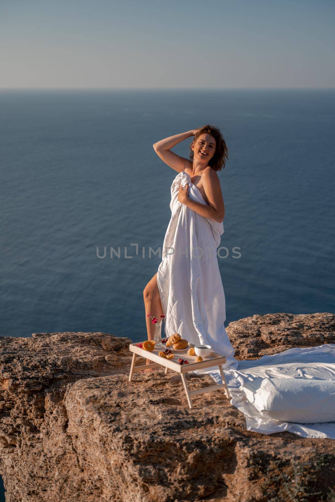 Woman wake up in bed wuth duvet and pillow over nature sea background outdoors. Back view. Good morning. Freedom concept