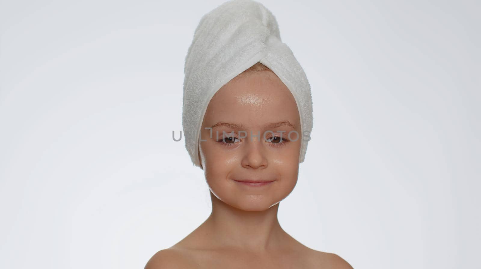 Lovely young child girl after bath in towel on head applying cleansing moisturizing cream. Teenager kid face skincare healthy treatment, natural creme cosmetics. Female portrait. Perfect fresh clean