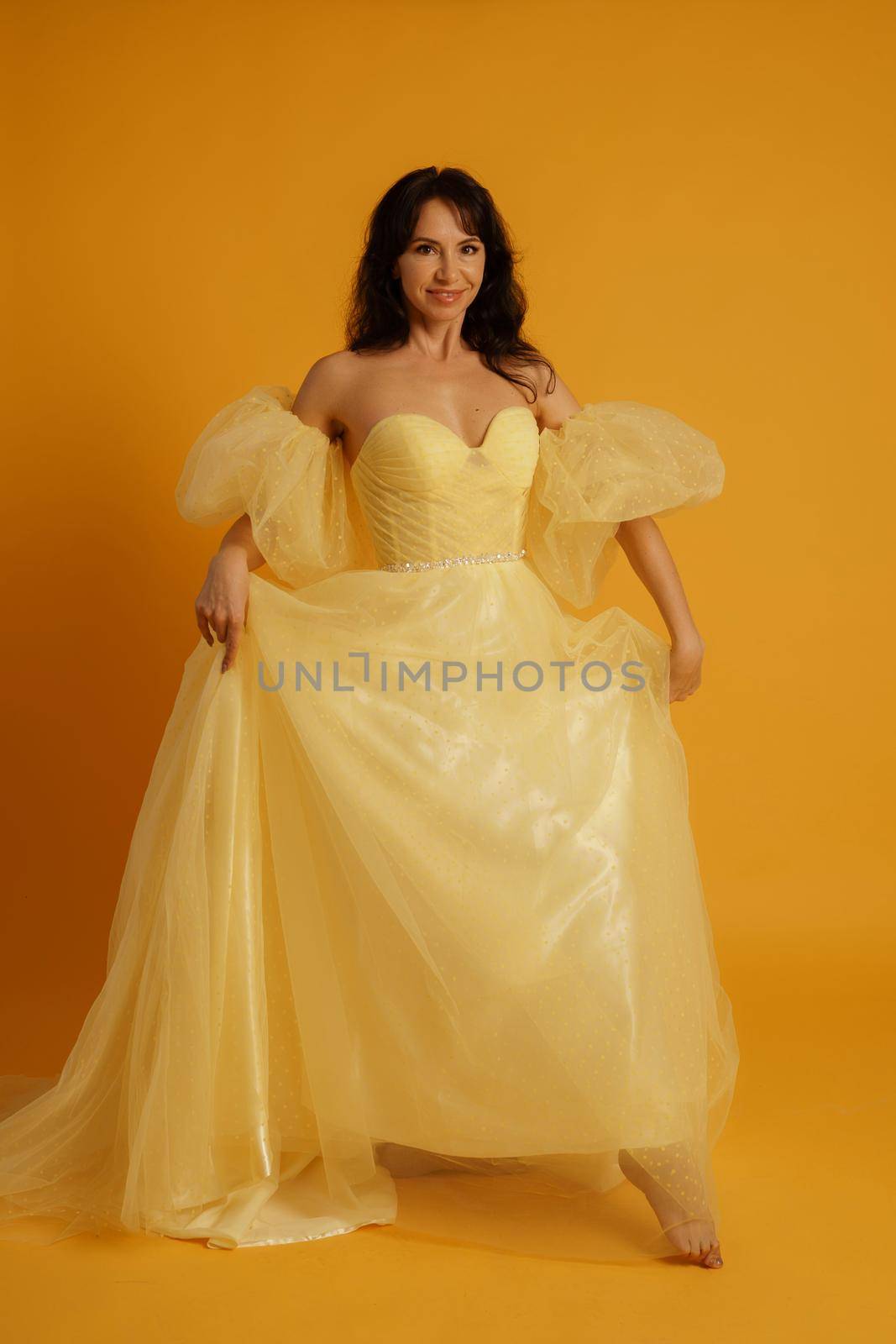 Portrait of a beautiful middle-aged woman in a yellow dress, her hair pulled up against a yellow background.