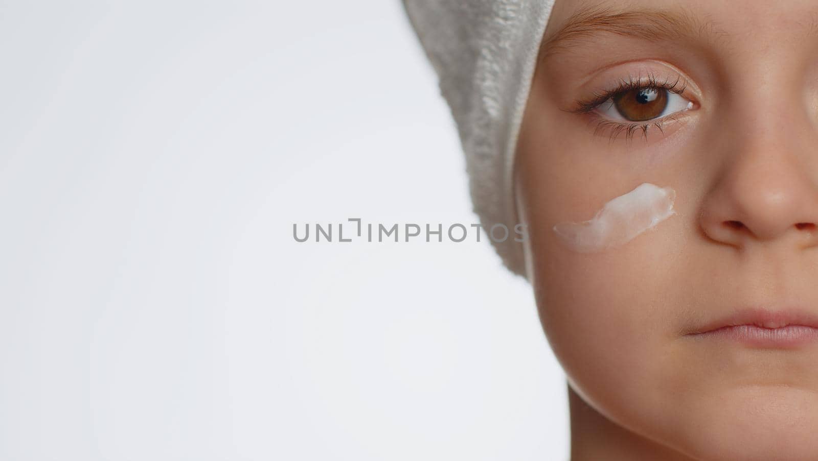 Close-up macro portrait of pretty young child girl applying cleansing moisturizing facial cream. Teenager kid face skincare healthy treatment, natural creme cosmetics. Perfect female fresh clean skin