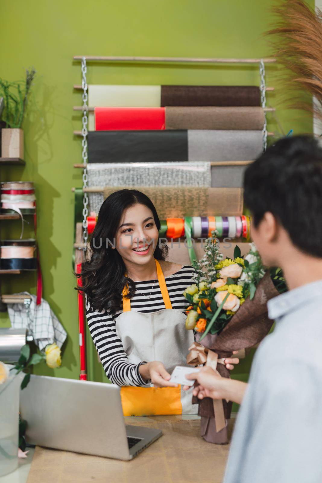 people, shopping, sale, floristry and consumerism concept - happy smiling florist woman making bouquet for and man or customer at flower shop