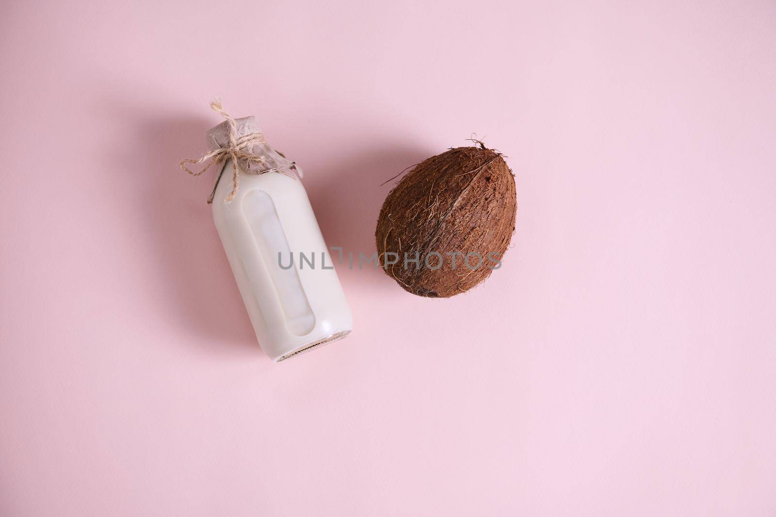 Flat lay composition with a bottle of a raw vegan, healthy organic plant based milk and a coconut, palm fruit isolated over pink background with copy space for advertising text