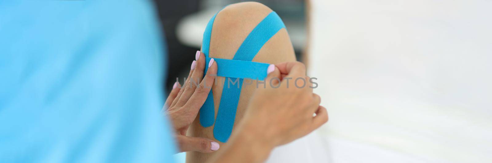 Doctor traumatologist gluing kinesio tapes on knee of female patient in clinic closeup by kuprevich