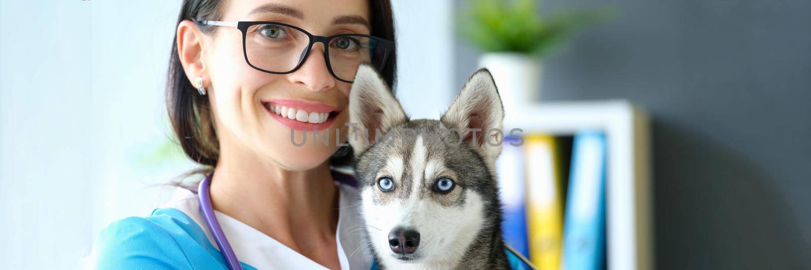 Smiling female veterinarian holding dog in her arms in clinic by kuprevich