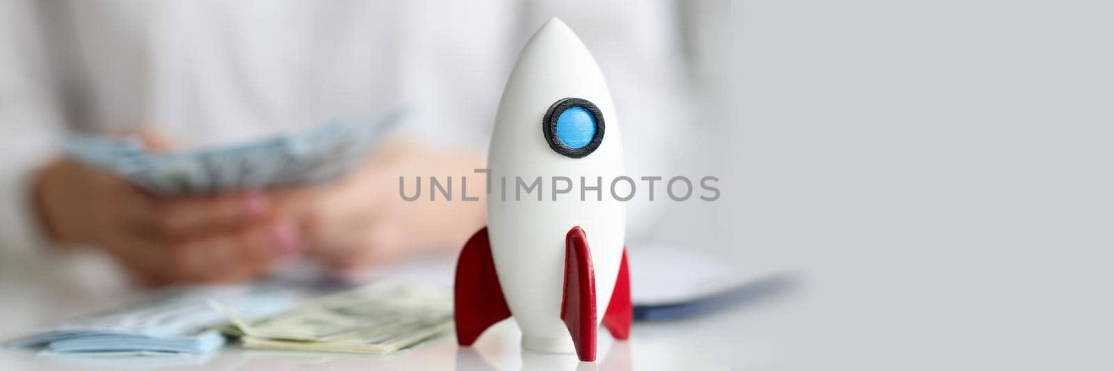 Toy rocket standing on table in front of woman with money closeup by kuprevich