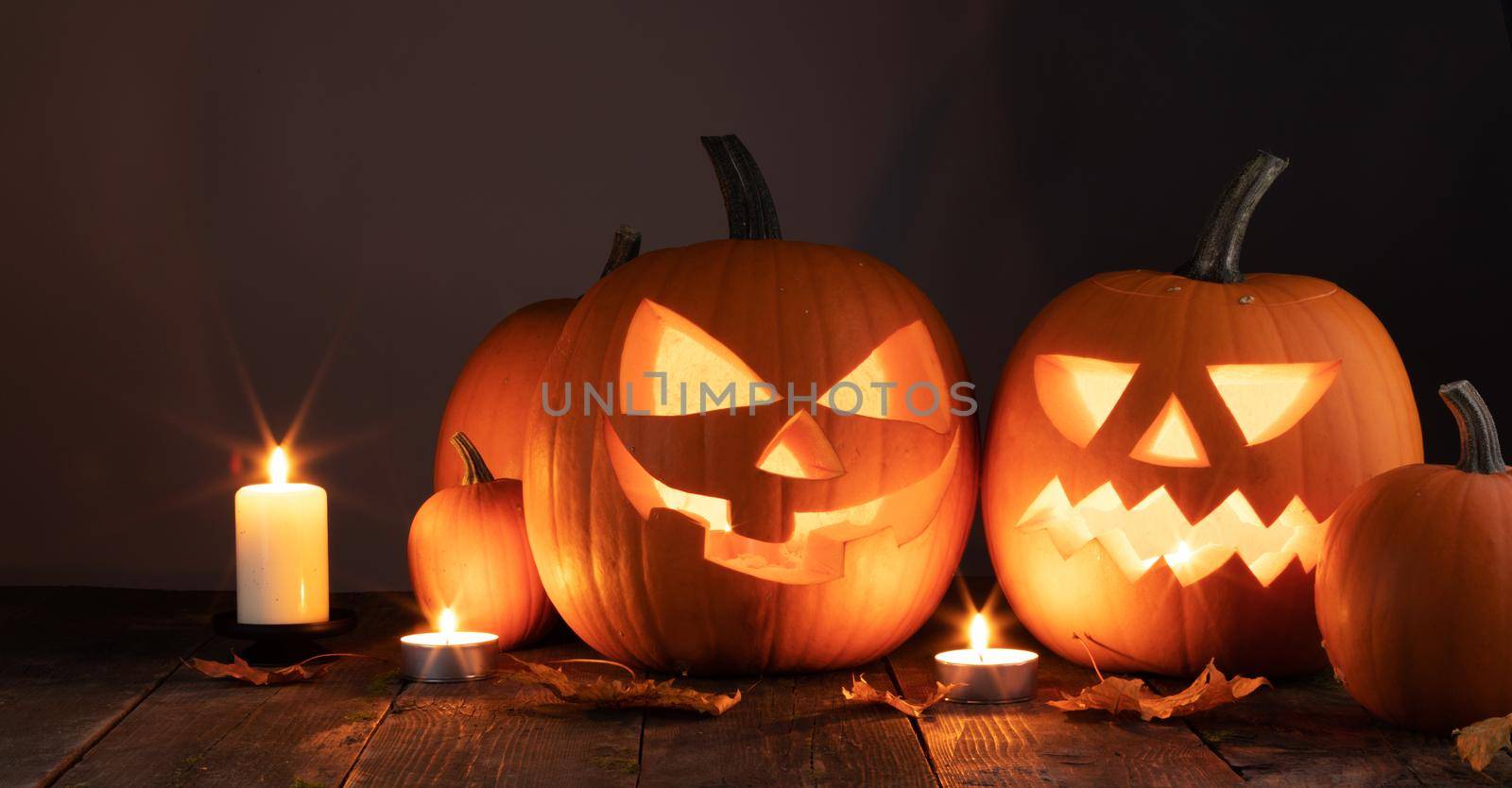 Halloween pumpkins candles and dry maple leaves on wooden background