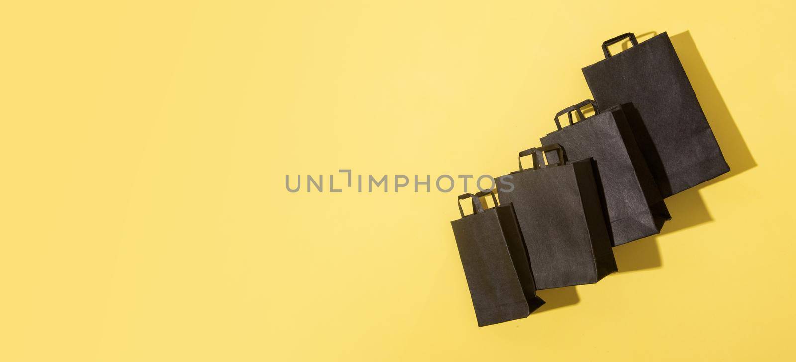 Black shopping bags on black friday sale yellow background with copy space. Banner format