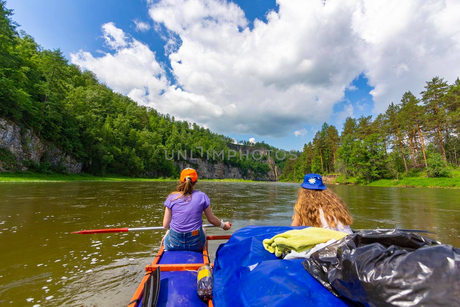 Two girls are rafting on an inflatable catamaran along the river among high rocks