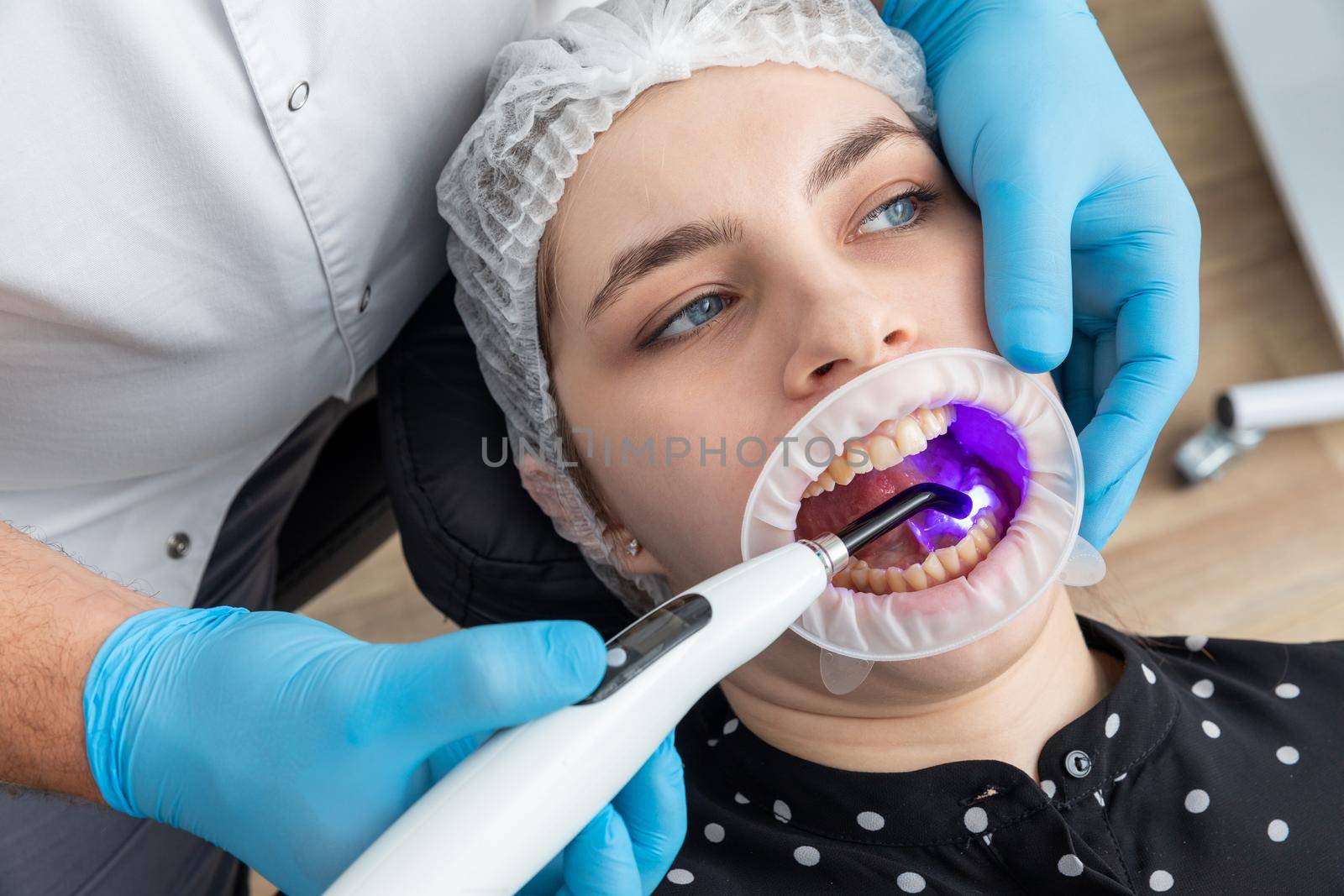 Closeup view of dentist using dental curing UV lamp on teeth of a patient