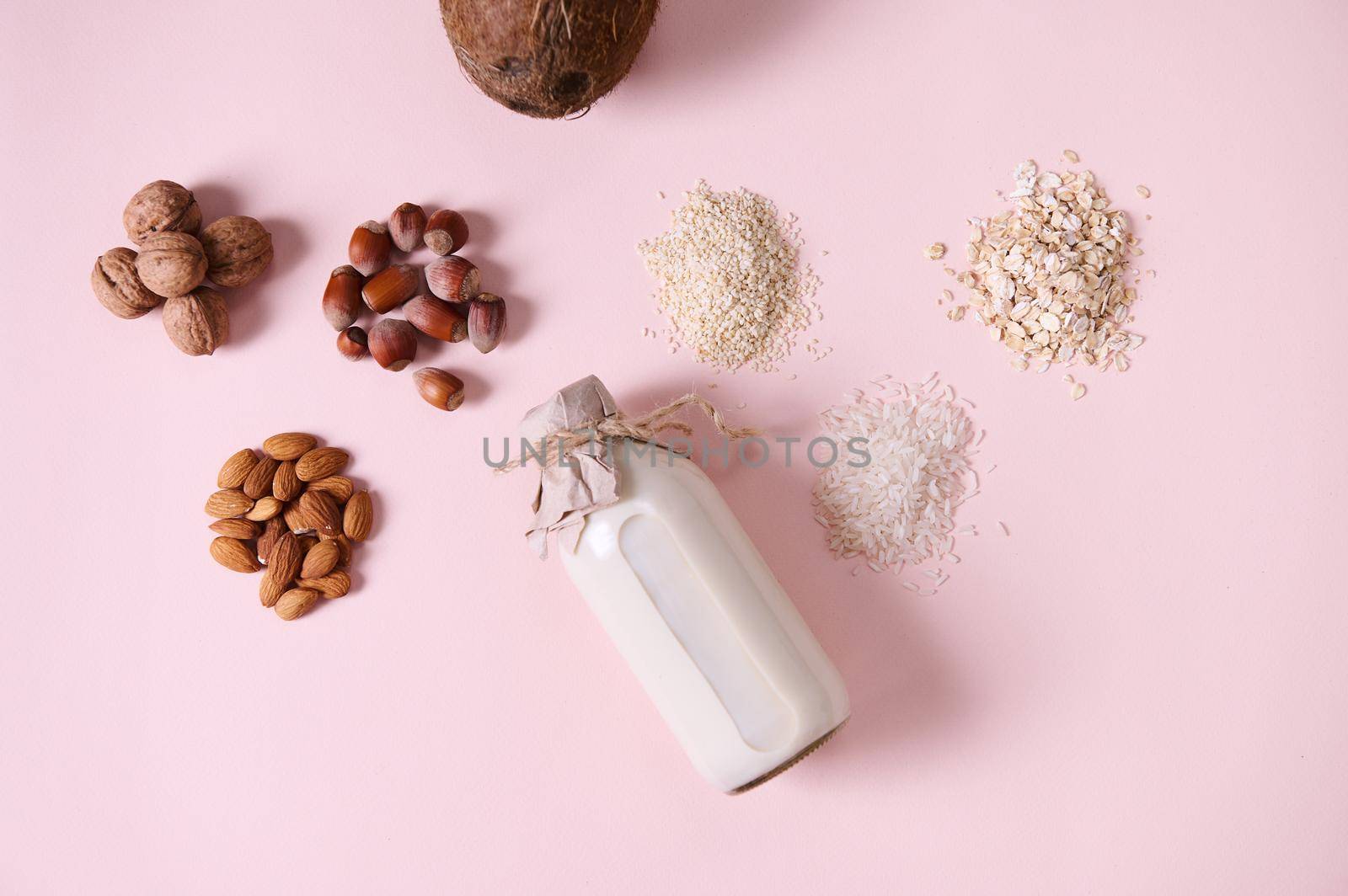 Flat lay food composition with a plant based milk and wholesome nuts, cereals and seeds on pink background. Copy space by artgf