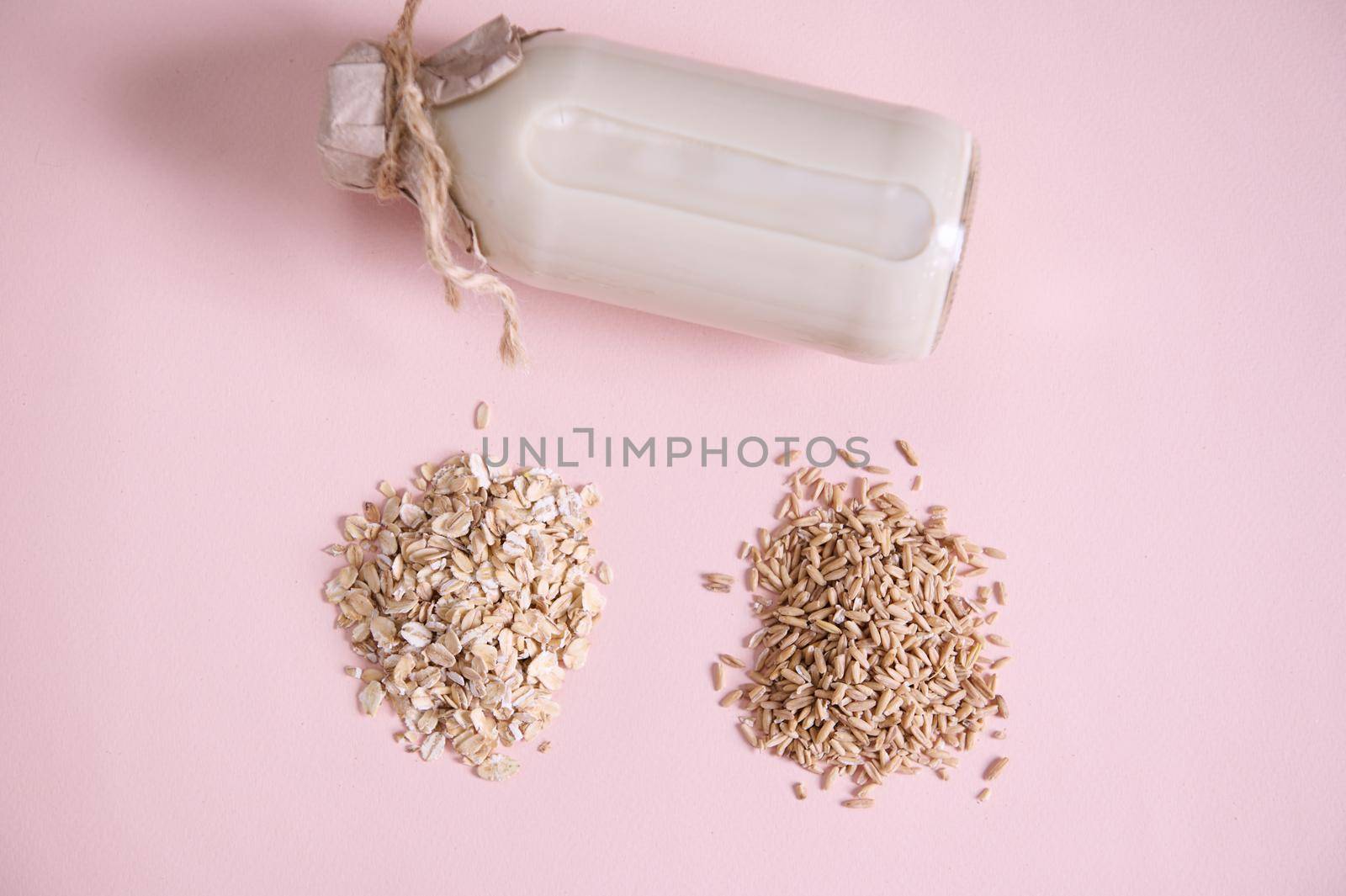 Flat lay Heap of oat groats, oat-flakes and bottle of plant based organic healthy vegan wholesome milk on pink surface. by artgf