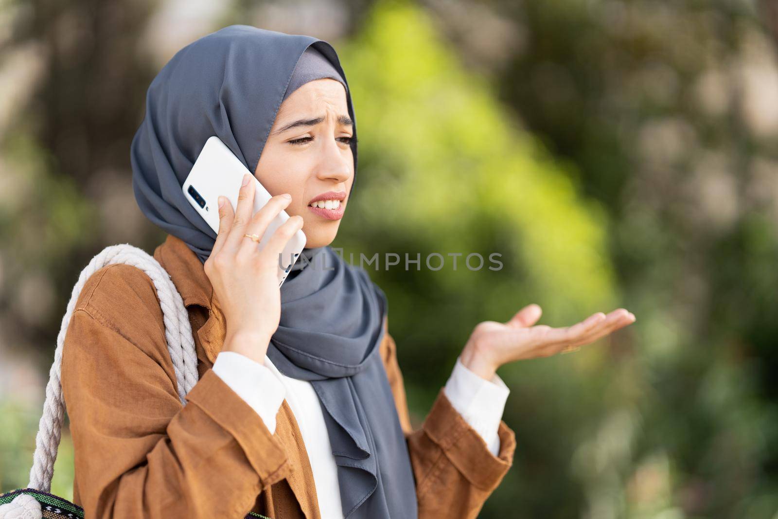 Muslim woman talking to mobile phone and gesturing misunderstanding