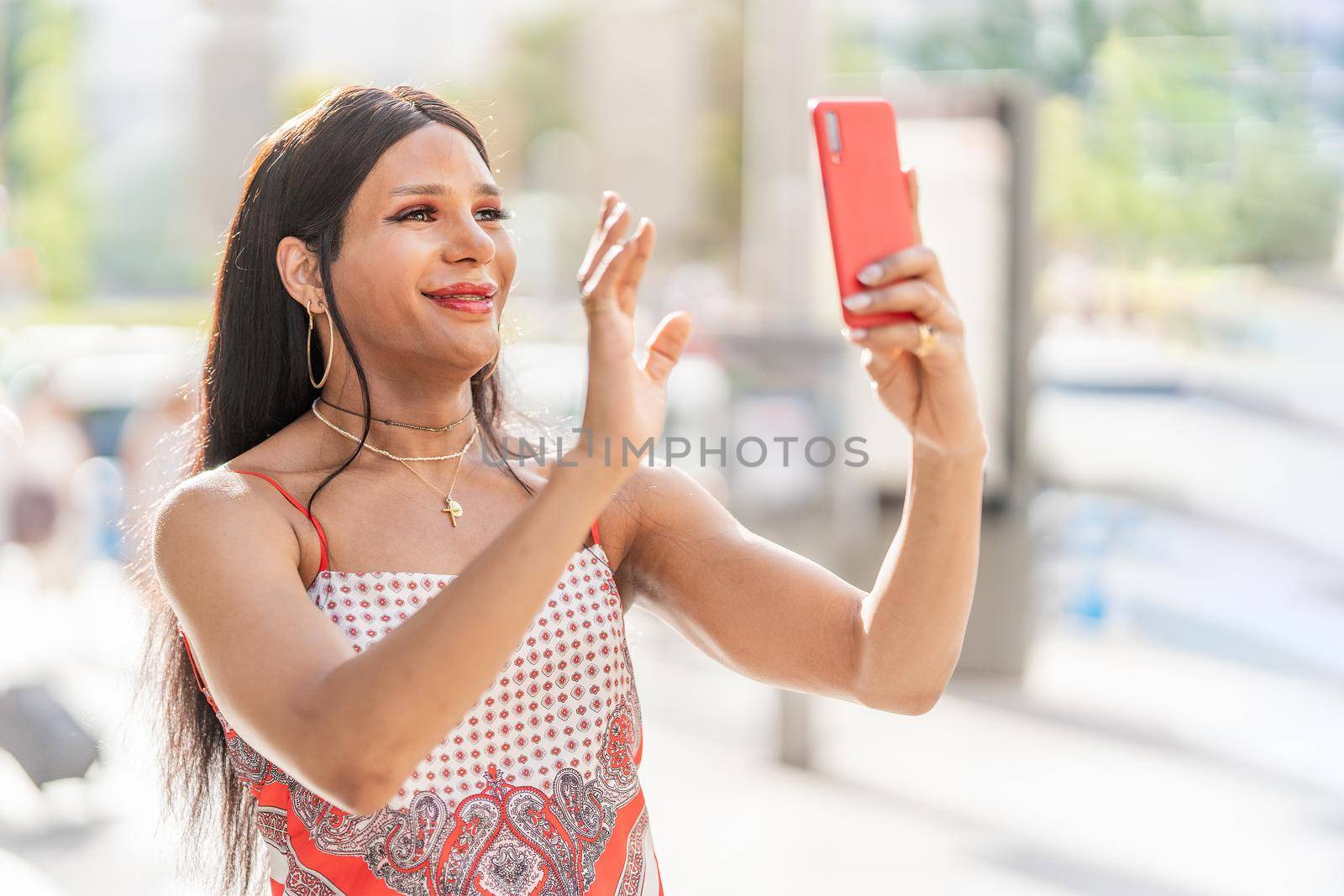 Trans woman waving at the mobile while doing a video call in the street in a sunny day of summer