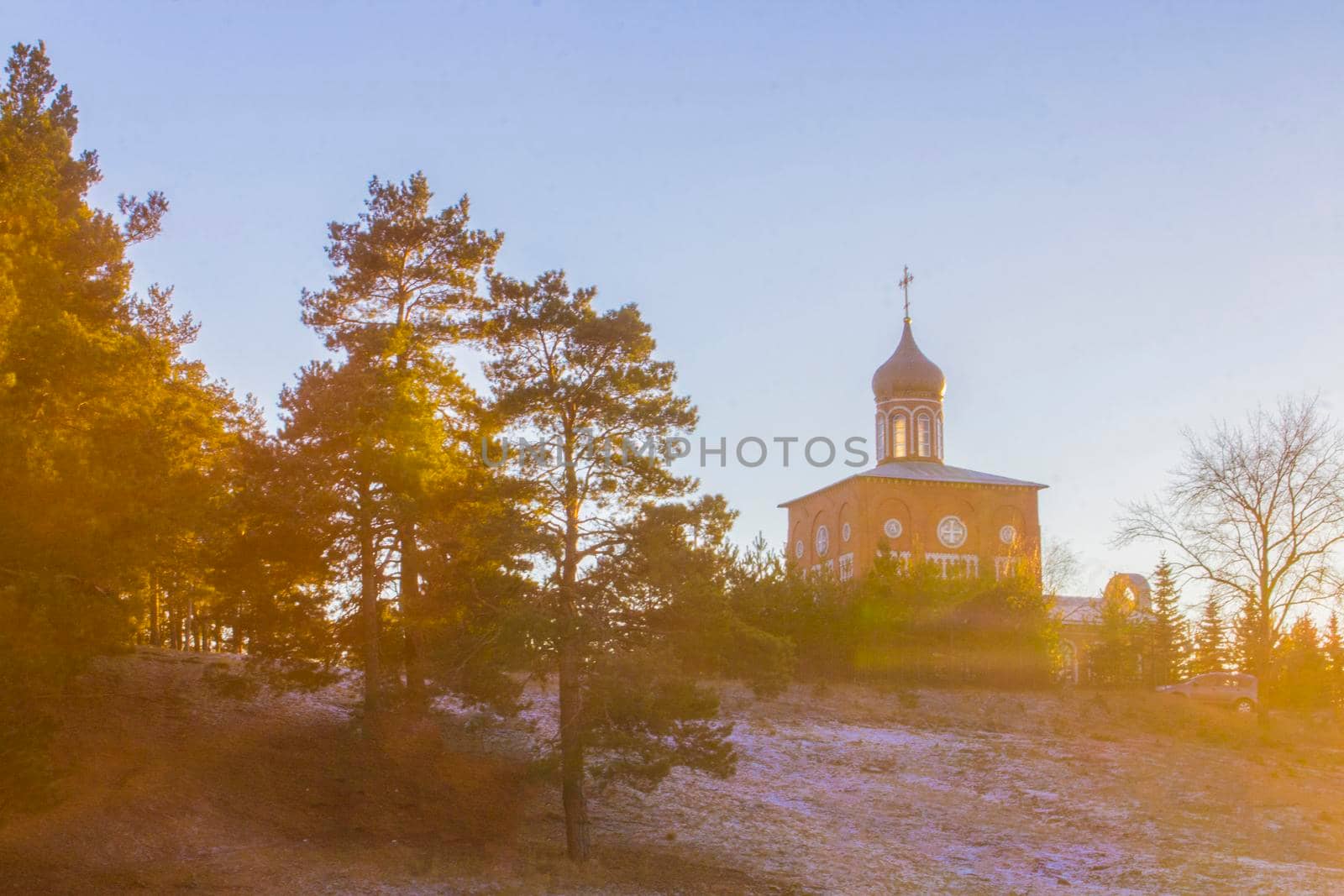 Orthodox church on a hill near the forest. Winter sunset landscape with clear blue sky.