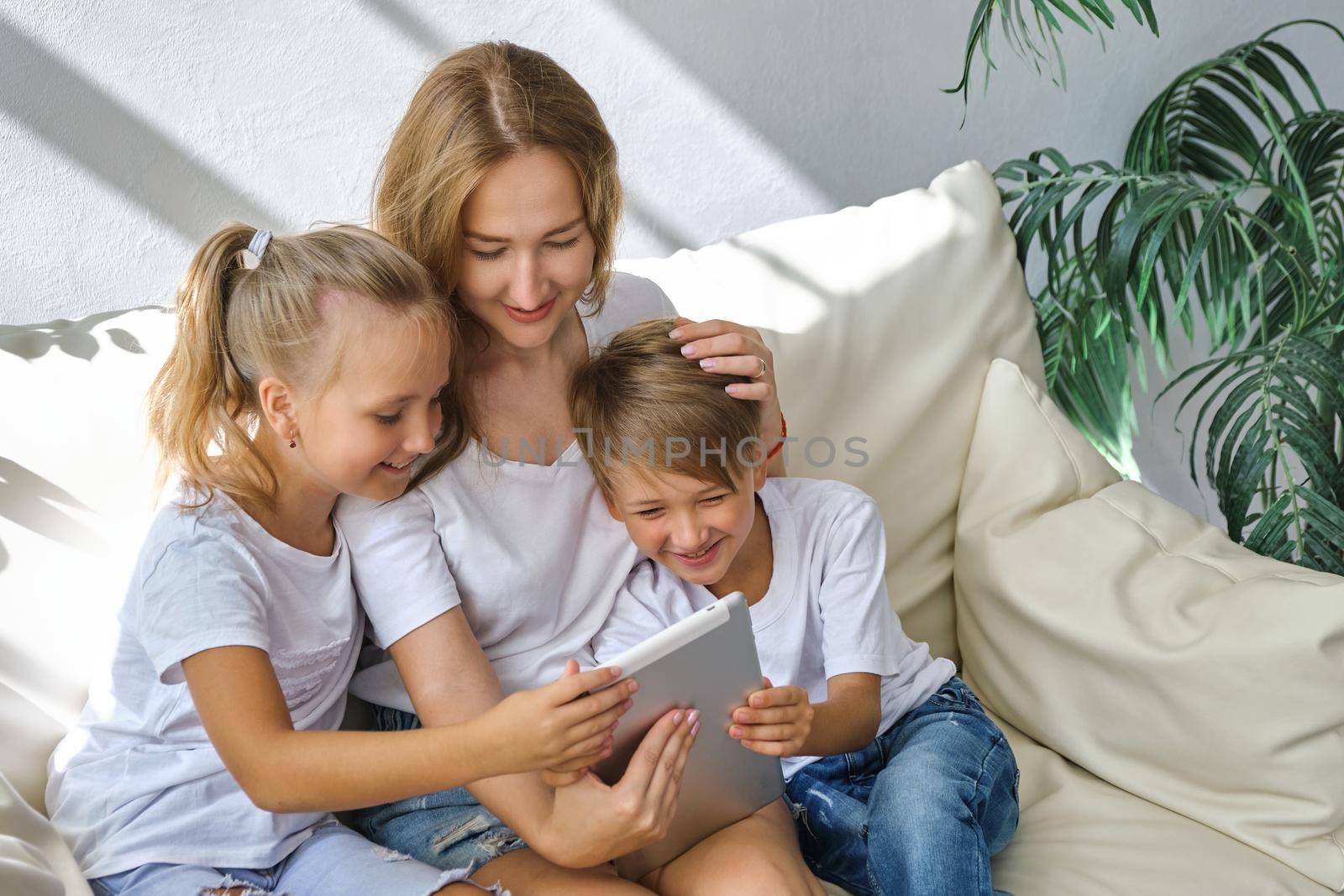 Family. Young mother with kids daughter and boy using digital tablet computer device. Caucasian family at home having online video conference call, rejoice and laugh.