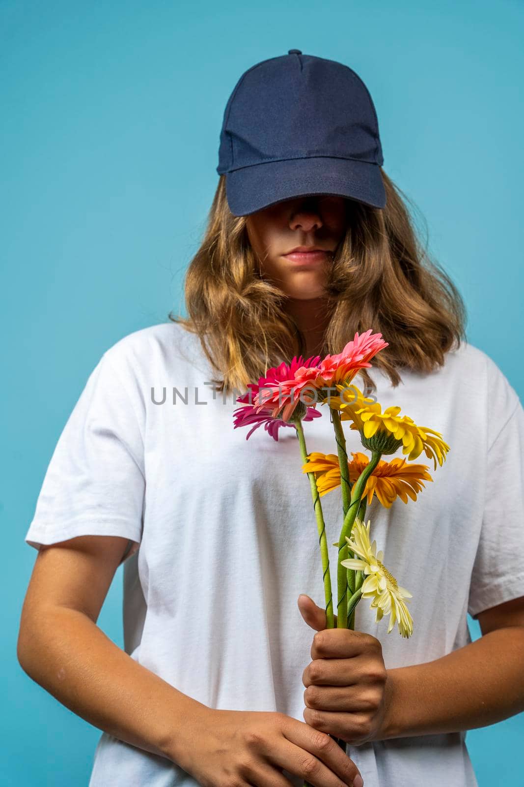 a girl with a bouquet of flowers in a white T-shirt and baseball cap on a blue background with a serious expression on her face. not a joyful teenage girl with flowers
