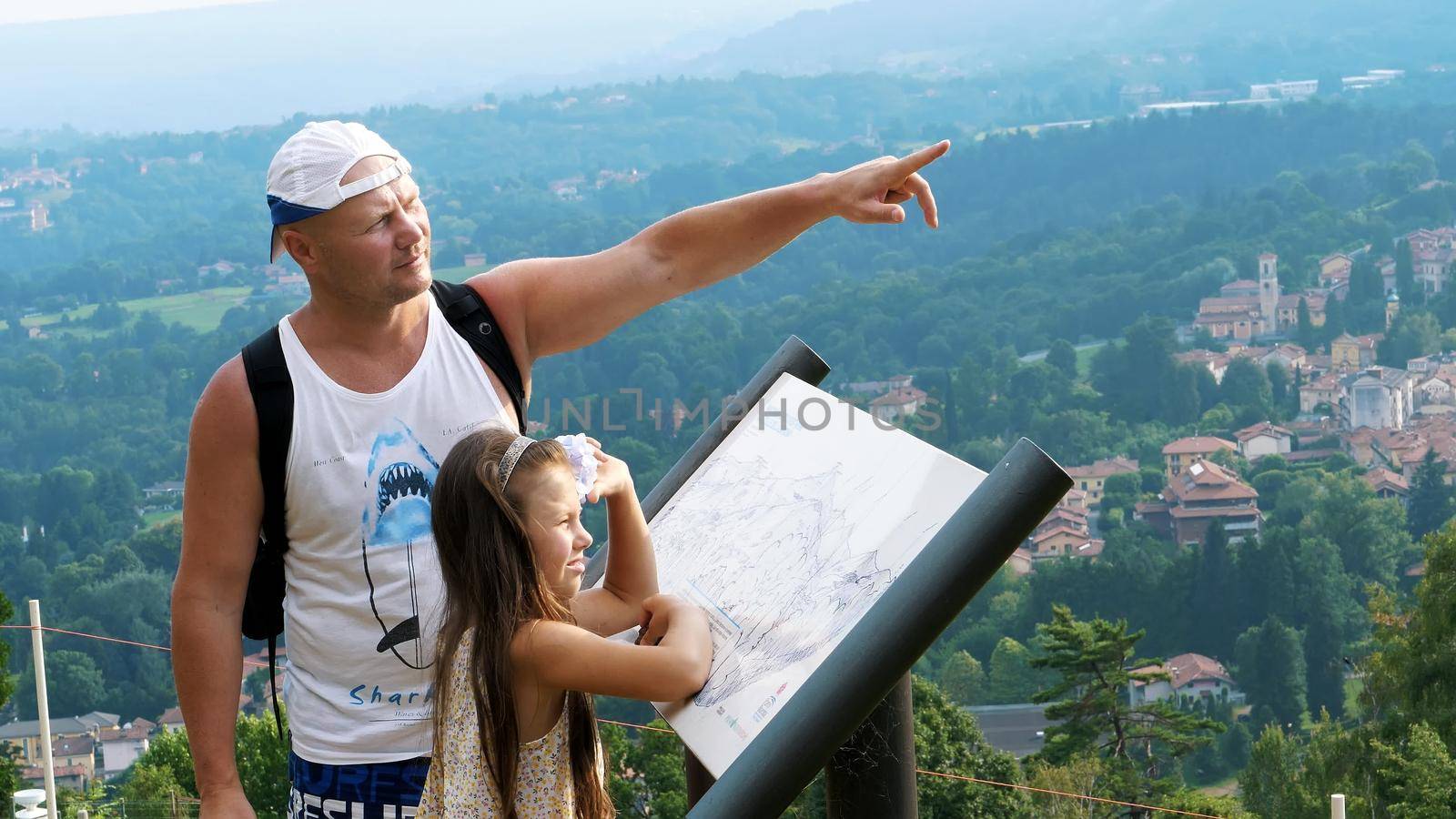 beautiful park in alpine mountains. man and a girl, kid, tourists, study map of park, against backdrop of picturesque landscape of the Alpine mountains and a small town. summer hot day. High quality photo