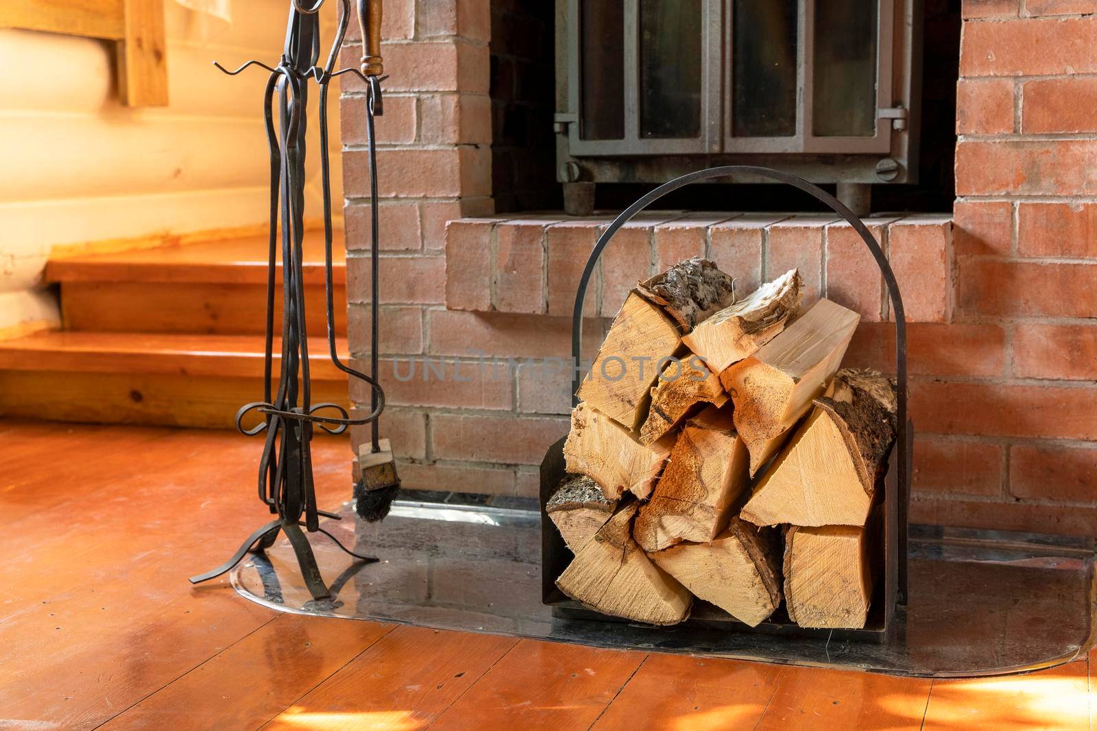 close-up of chopped wooden firewood stacked in a beautiful iron woodpile against the background of a beautiful brick fireplace. fireplace care items, poker, shovel, tongs