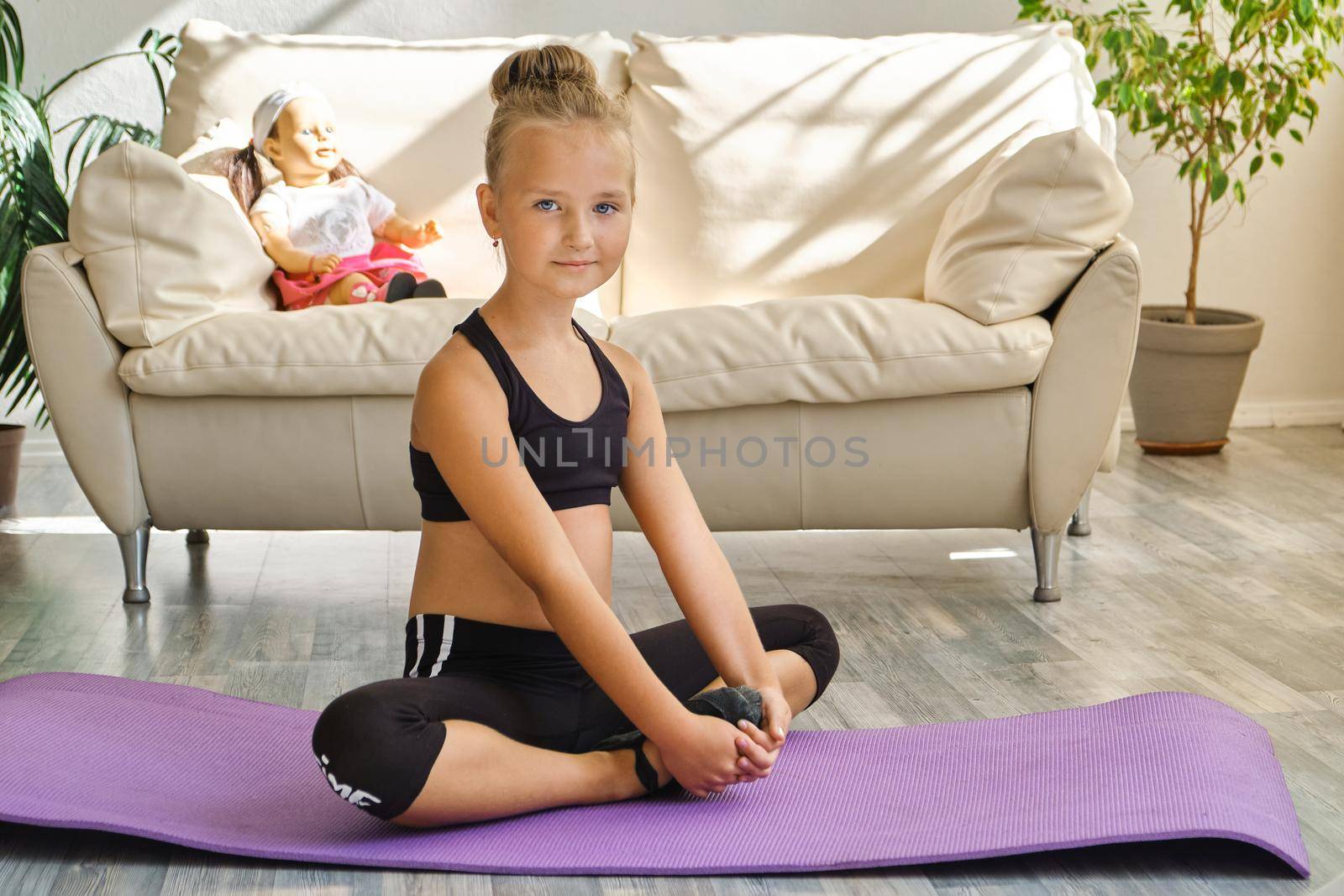 Little cute girl is practicing gymnastics at home. Video lesson. Kid repeating exercises while watching online yoga gymnastics session. Beautiful girl doing fitness exercise at home