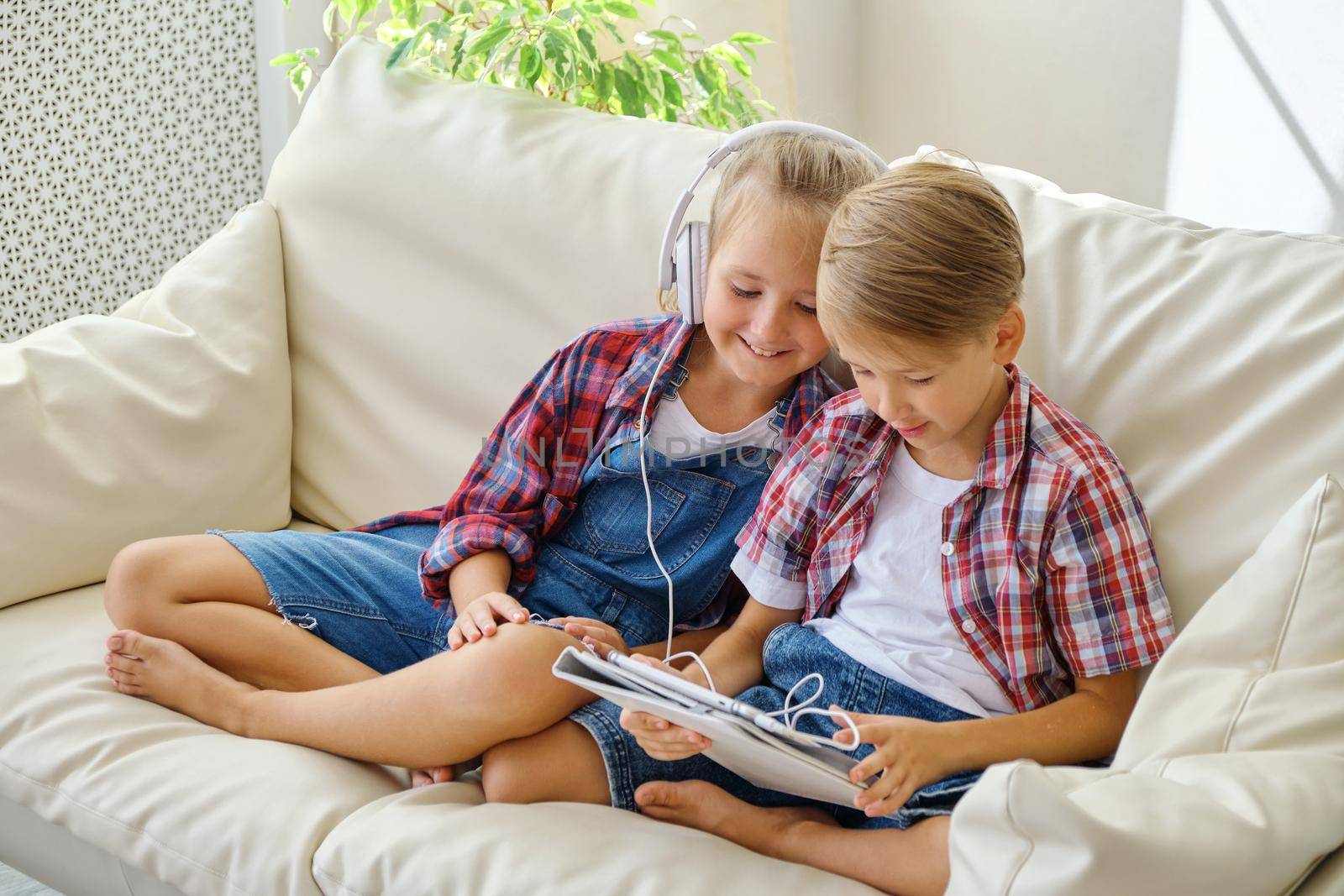 Cute brother and sister with headphones enjoying tablet at home. family, children, technology and home concept