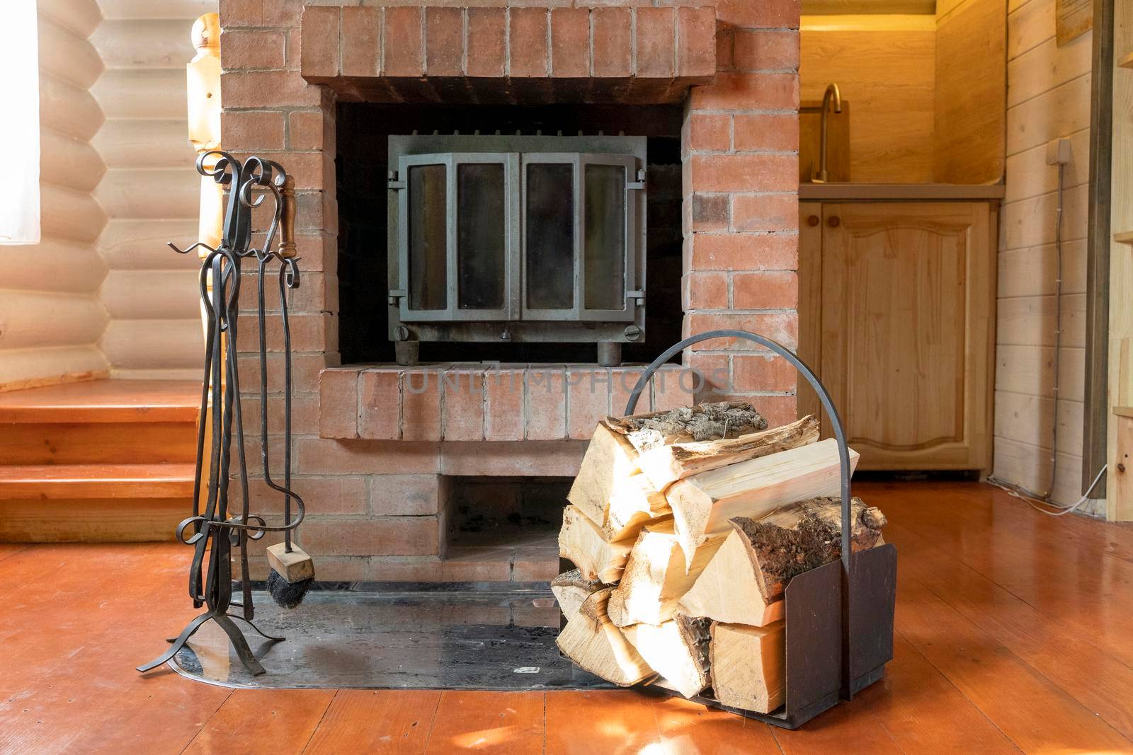 close-up of chopped wooden firewood stacked in a beautiful iron woodpile against the background of a beautiful brick fireplace. fireplace care items, poker, shovel, tongs