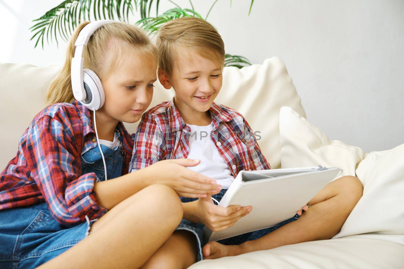 Cute brother and sister with headphones enjoying tablet at home. family, children, technology and home concept